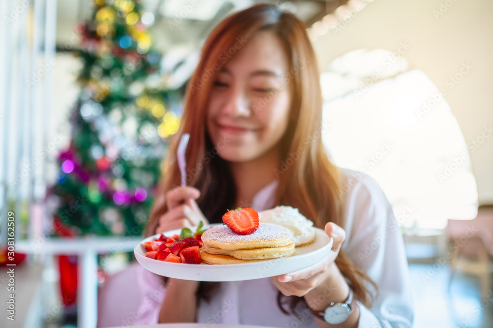 A beautiful asian woman holding and eating pancakes with strawberries and whipped cream by fork