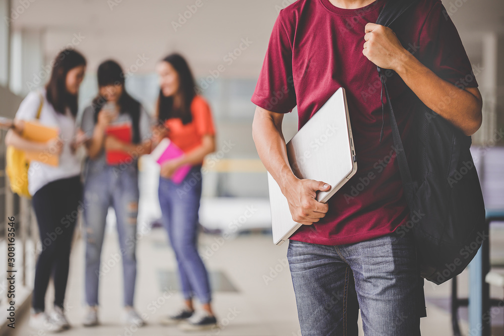 Obraz premium Education concept - Teens in the university and modern technology. Close up holding hand student a laptop and group of friends standing in the back.