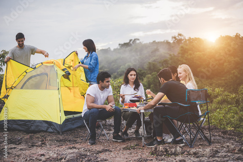 Camping concept - Happy friends are grilling and cooking at the camp next to nature and mountains.