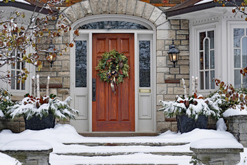 Front door of snow covered house with Christmas wreath
