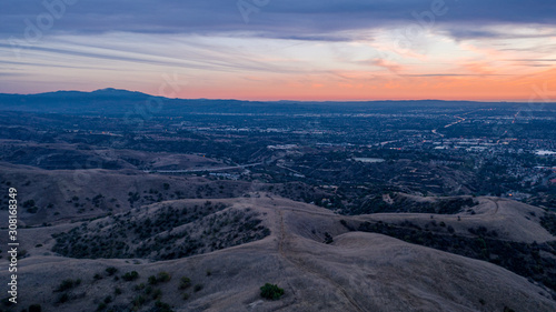 Aerial view of open rolling hills in suburban Southern California. Radio tower atop hill during sunset surrounded by mountains and ocean