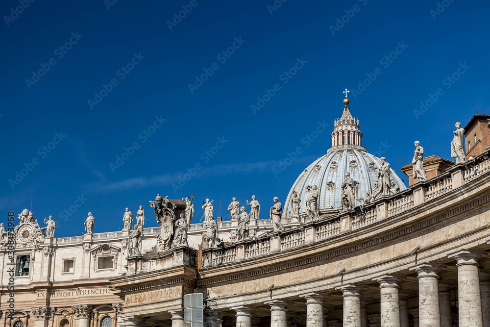 View of the colonnade, pediment and the dome of St. Peter's Basilica in the Vatican against the blue sky.