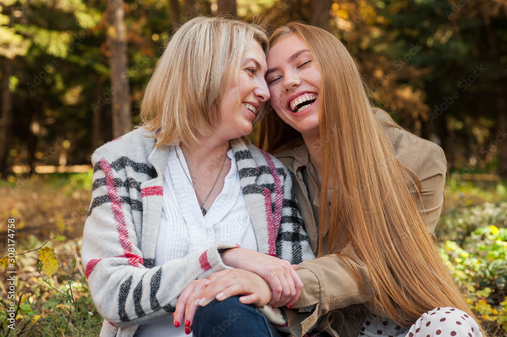 Fototapeta premium Happy adult daughter hugs her mom sitting in summer park, they are laughing. Tender and caring relationships of children and parents