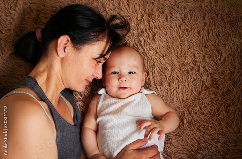 Young mother gently hugs her 6 month old baby in bed, top view copy space. Happy childhood, motherly love