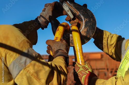 Construction male rigger hands wearing a heavy duty safety glove protection while clipping lifting and inspecting crane hook on open field construction site   