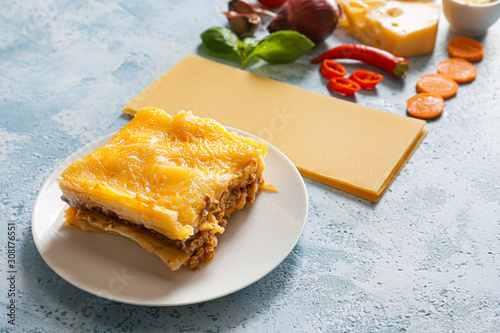 Plate with tasty baked lasagna and ingredients on color background