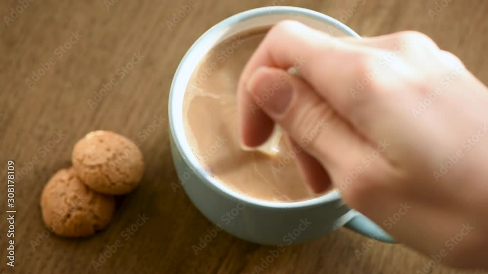 Female hand adding spoon of brown sugar into coffee with milk and stirring it with a spoon Female hand adding spoon of brown sugar into coffee with milk and stirring it with a spoon