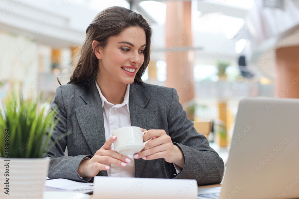 Attractive smiling businesswoman sitting in the office with a cup of coffee. Attractive smiling businesswoman sitting in the office with a cup of coffee.