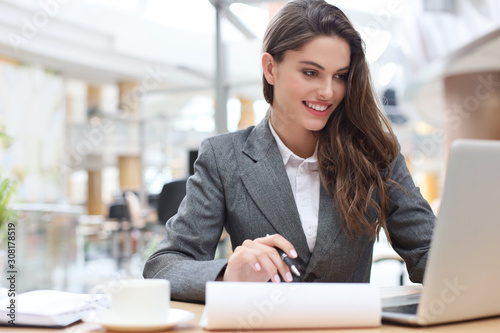 Portrait of a young brunette business woman using laptop at office.