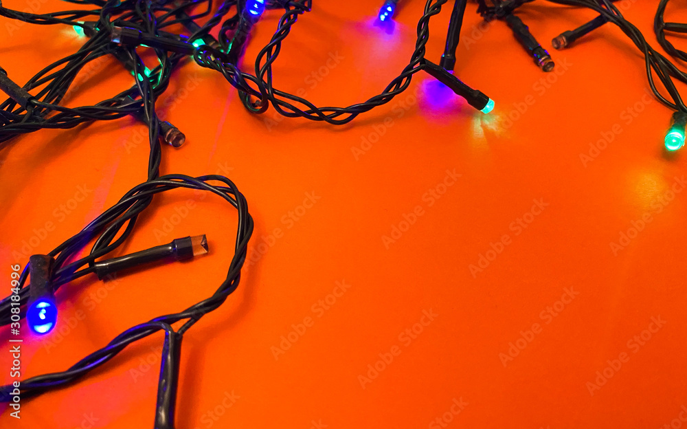 Christmas garland sparkles with colored lights on an orange background. Copy space. Christmas garland sparkles with colored lights on an orange background. Copy space.