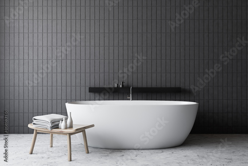 Gray tile bathroom with white tub and chair