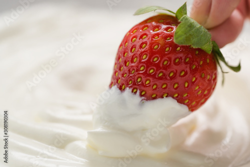 Closeup hand dips strawberry in white cream or yogurt