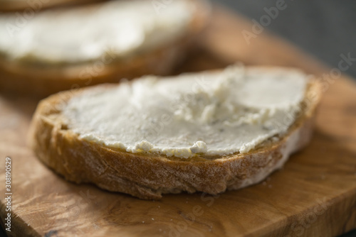 Closeup of three ciabatta slices with cream cheese on olive wood board on terrazzo surface