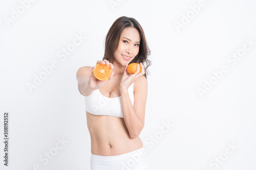 Smiling woman holding orange juice and fruit. Muscular woman's body in white lingerie isolated on white background.