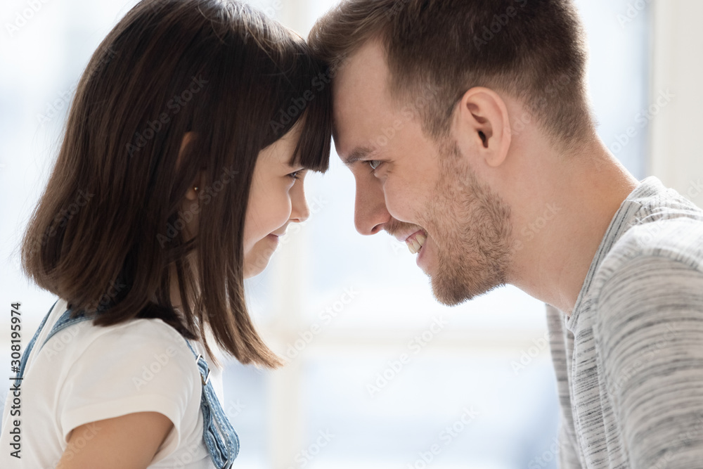 Close up adorable little daughter and father touching foreheads. Close up adorable little daughter and father touching foreheads.