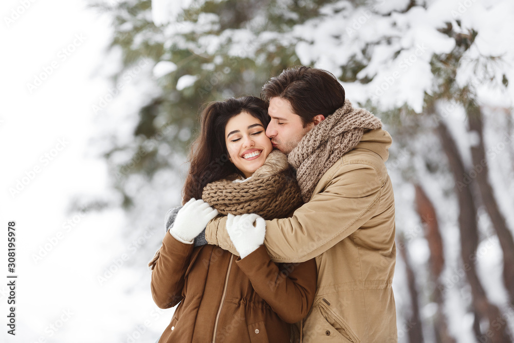 Man Kissing Girlfriend In Cheek Hugging In Snowy Forest Man Kissing Girlfriend In Cheek Hugging In Snowy Forest