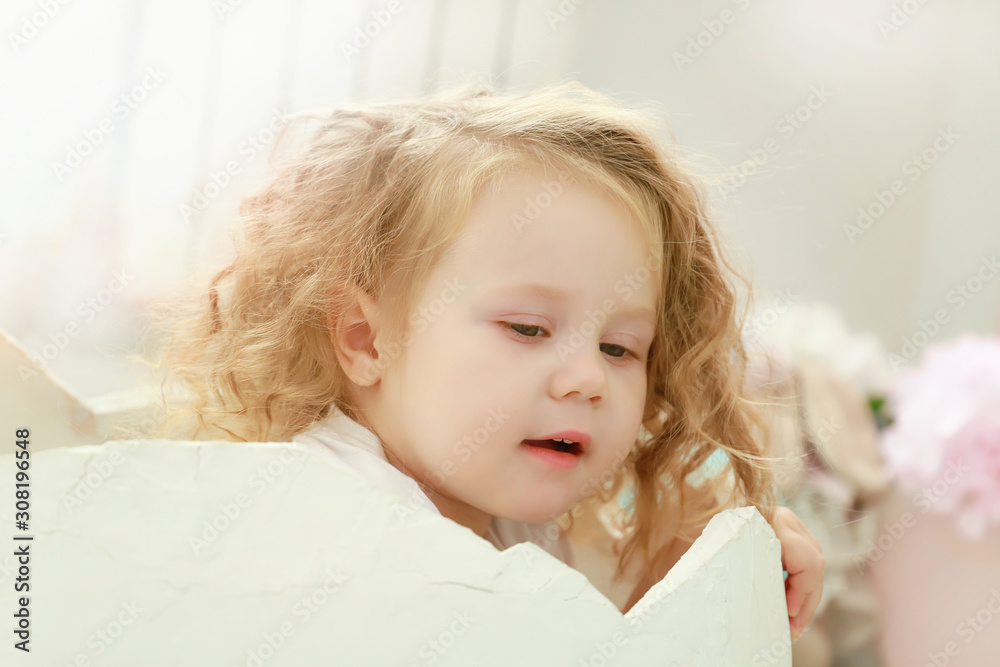 A little toddler kid is sitting in a white egg that hatched against a studio colorful background for a newborn portrait or family concept.