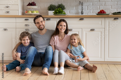 Family with kids hugging sitting on warm floor in kitchen