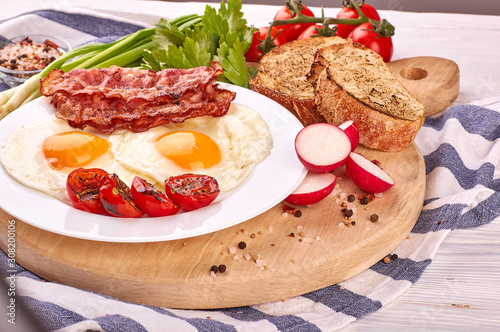 fried eggs on a wooden table, accompanied by fresh green parsley, cherry tomatoes on a branch, with fried crispy bacon and toasted baguette.