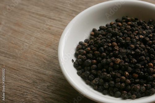 Black pepper in a plate on a wooden background. 