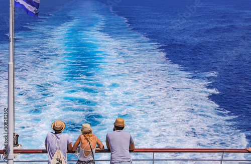 Tourists with a straw hat stand on the deck of a cruise ship and look out over the ocean  While the boat is sailing.
