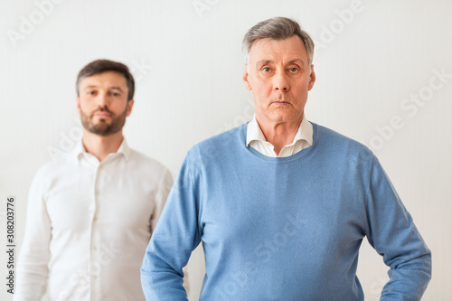 Mature Son Standing Overshadowed By His Elderly Father, White Background