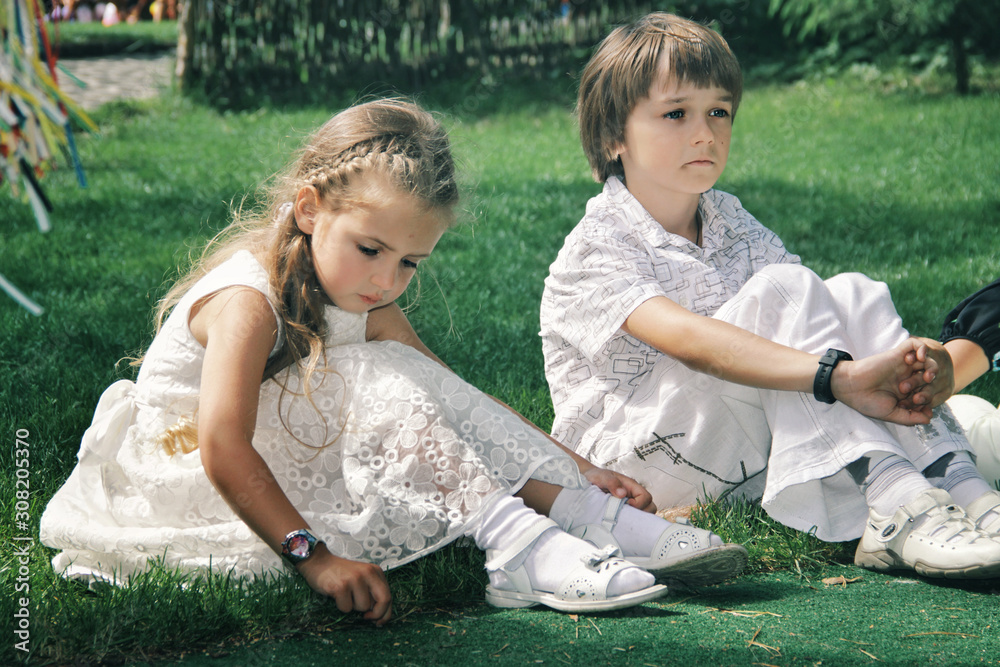 Portrait of little caucasian girl and boy in casual clothes sitting on the grass