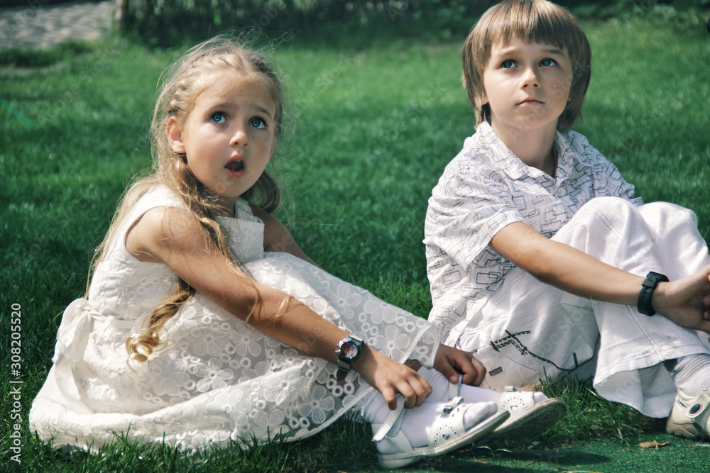 Portrait of little caucasian girl and boy in casual clothes sitting on the grass