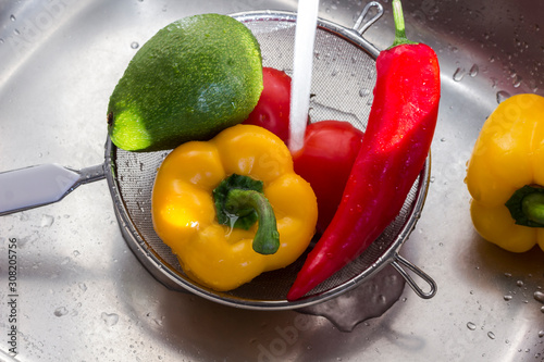 red and yellow peppers in a colander under a stream of water, diet food concept photo