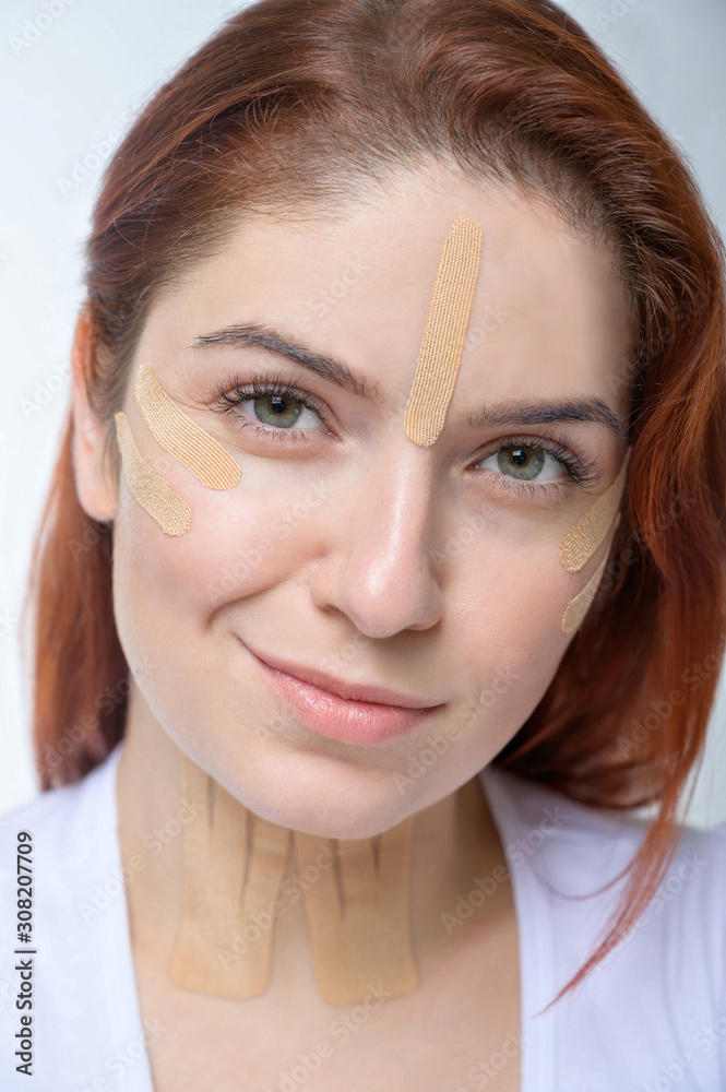 Portrait of a redhead woman with tapes on skin color face for rejuvenation. An alternative way to fight wrinkles. Portrait of a redhead woman with tapes on skin color face for rejuvenation. An alternative way to fight wrinkles.