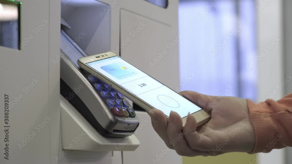 adult woman uses NFC contactless payment application on her smartphone to pay for order in fastfood. female buyer applies phone with NFC application to pos-card reader at terminal in store making paym