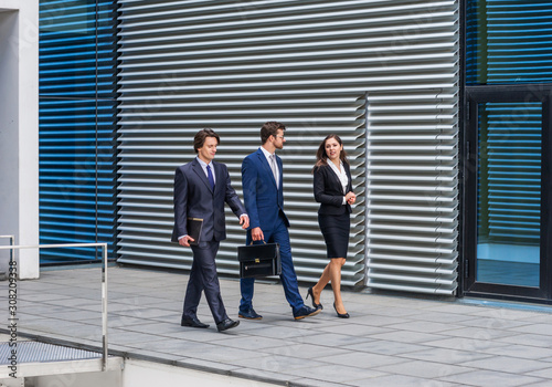 Confident businesspersons talking in front of modern office building. Businessmen and businesswoman have business conversation. Banking and financial market concept.