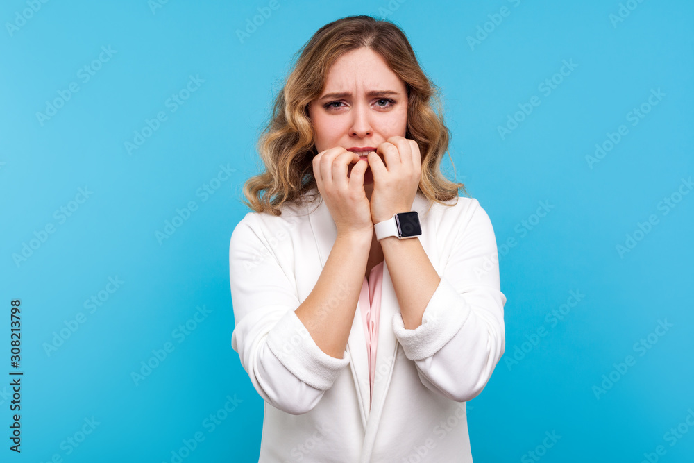 Depression and anxiety. Portrait of worried woman with wavy hair in white jacket biting nails looking frightened terrified about problems, nervous disorder. studio shot isolated on blue background Depression and anxiety. Portrait of worried woman with wavy hair in white jacket biting nails looking frightened terrified about problems, nervous disorder. studio shot isolated on blue background