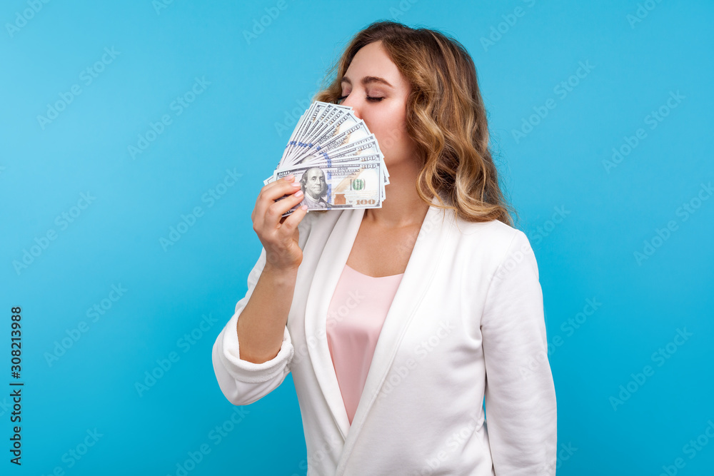 Portrait of wealthy greedy woman with wavy hair in white jacket sniffing dollars and closing eyes with pleasure, enjoying lottery win, investment income, money profit. studio shot, blue background Portrait of wealthy greedy woman with wavy hair in white jacket sniffing dollars and closing eyes with pleasure, enjoying lottery win, investment income, money profit. studio shot, blue background