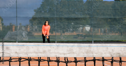 Young woman playing tennis. Girl is practicing tennis. Sports training of children. Focus on the net. The girl in the background is intentionally out of focus..