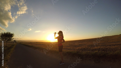 Running at sunset. A young woman drinking water during a running exercise. (Intentionally uneven horizon line - fish eye effect)