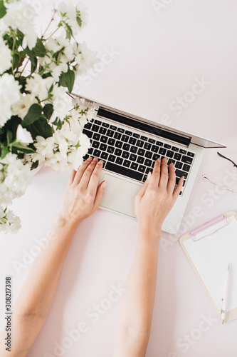 Woman works on laptop. Freelancer co-working office desk workspace with flowers bouquet and stationery on white table. Flat lay, top view business hero header background.