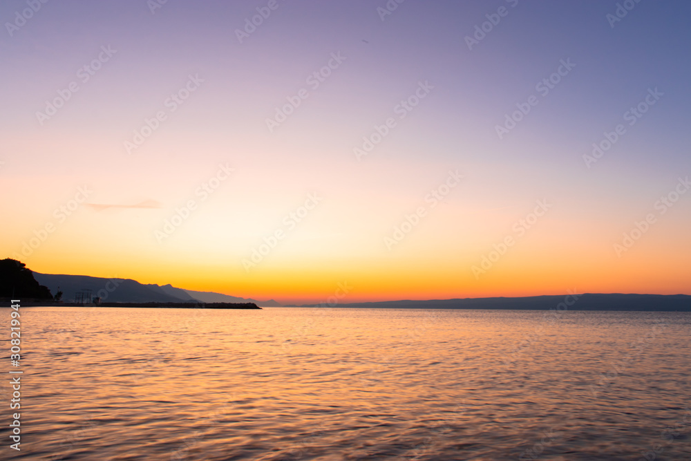 Obraz premium Dark beach at a sunrise with golden white orange sky. Beach in split,croatia