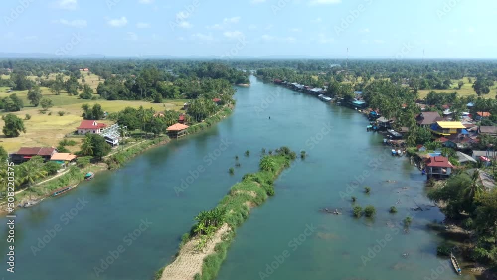 Four Thousand Islands In Mekong, Laos - Lush Islet In The Middle Of The Long Shallow River With Green Trees And Houses Alongside Under The Blue Sky - Aerial Drone Shot Four Thousand Islands In Mekong, Laos - Lush Islet In The Middle Of The Long Shallow River With Green Trees And Houses Alongside Under The Blue Sky - Aerial Drone Shot