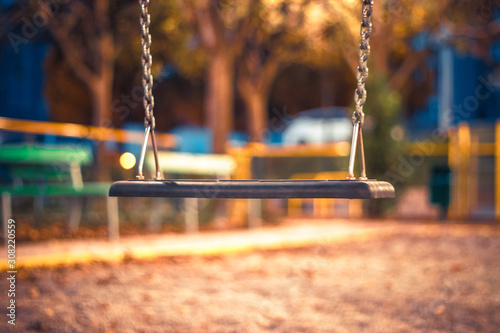 An empty  swin hang at the playground. No children are playing on the swing set, which is not moving. The swings are clean and well maintained. Back to School. Recess equipment. Outdoors.