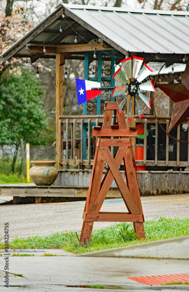 Texas miniature sized windmill with Texas flag and star on wind fan in front of a house with giant rustic star near the 