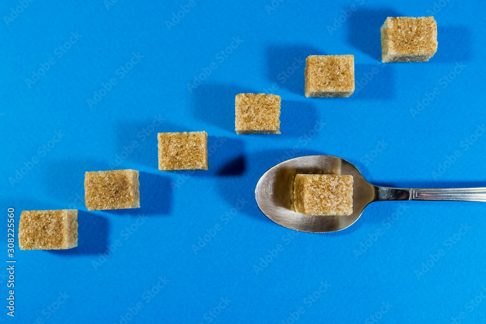 Brown sugar cubes in row focus on the cube in the spoon on blue