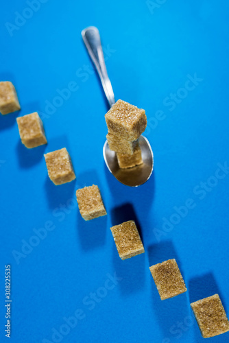 Fototapeta Naklejka Na Ścianę i Meble -  Vertical image of brown sugar cubes in row, focus on the cubes in the spoon on blue background.