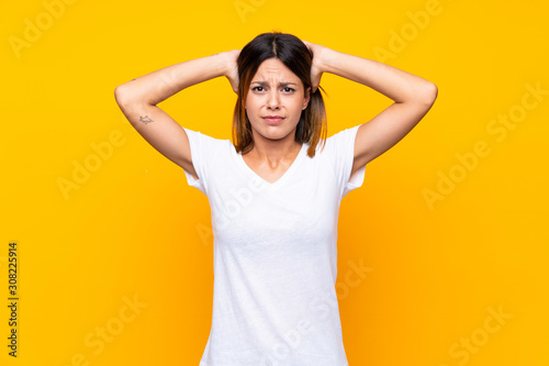 Young woman over isolated yellow background frustrated and takes hands on head