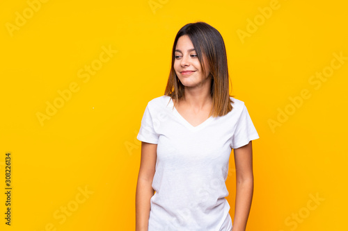 Young woman over isolated yellow background making doubts gesture looking side