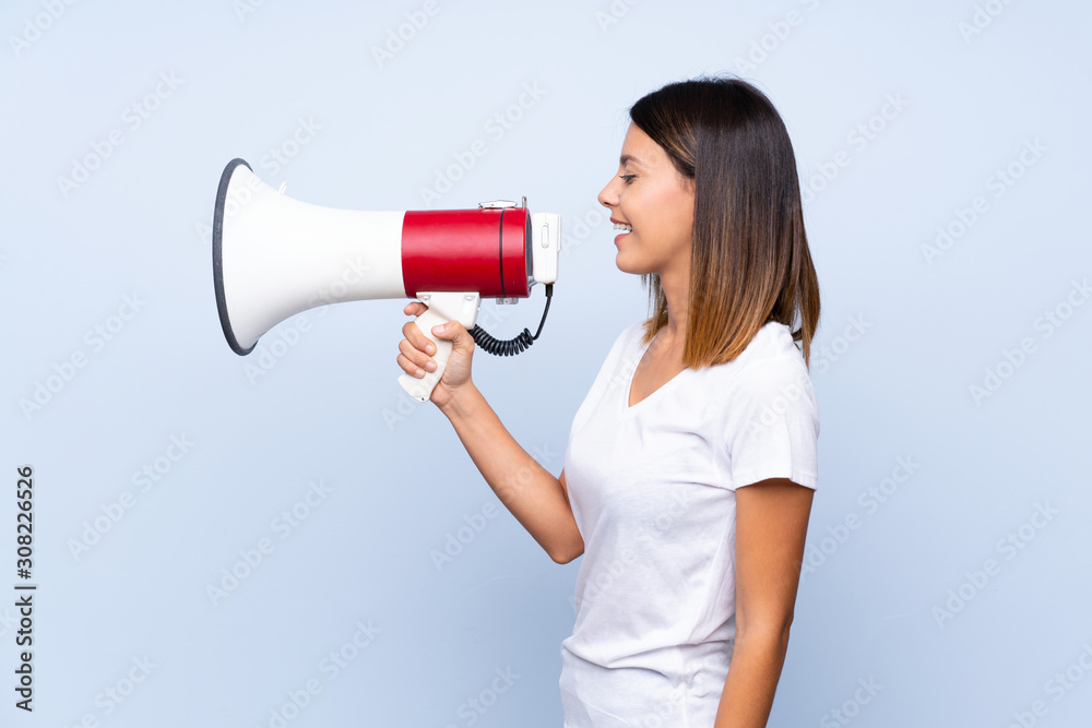 Young woman over isolated blue background shouting through a megaphone Young woman over isolated blue background shouting through a megaphone