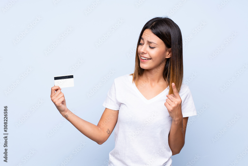 Young woman over isolated blue background holding a credit card Young woman over isolated blue background holding a credit card