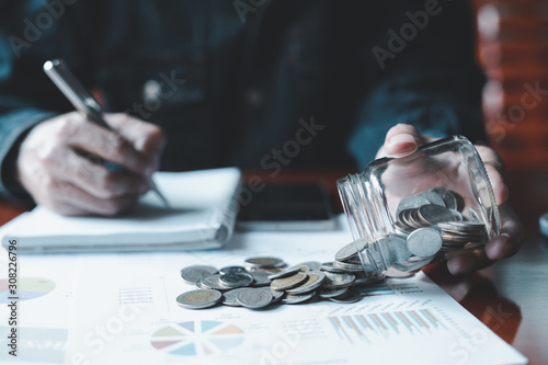 Man is taking notes of saving money in a notebook, with a money jar and a business report on the table.