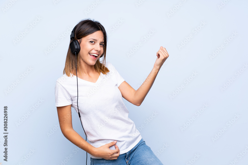 Young woman over isolated blue background using the mobile with headphones and dancing Young woman over isolated blue background using the mobile with headphones and dancing