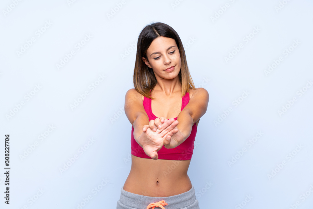 Young sport woman over isolated blue background stretching arm Young sport woman over isolated blue background stretching arm